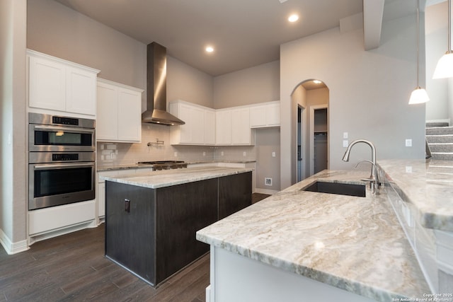 kitchen featuring light stone counters, stainless steel appliances, a sink, wall chimney range hood, and tasteful backsplash