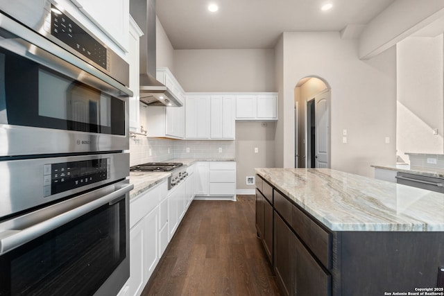 kitchen with arched walkways, stainless steel appliances, backsplash, light stone countertops, and dark wood-style floors