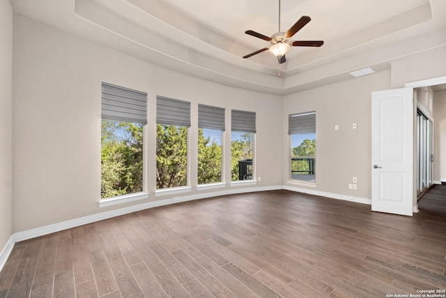 spare room featuring a ceiling fan, baseboards, a raised ceiling, and dark wood-type flooring