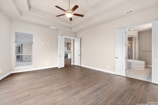 unfurnished bedroom featuring visible vents, baseboards, dark wood-style floors, a tray ceiling, and ensuite bath