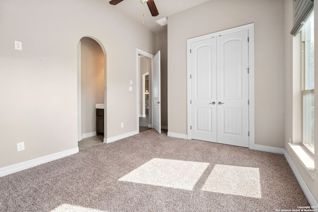 unfurnished bedroom with carpet floors, baseboards, arched walkways, and a closet