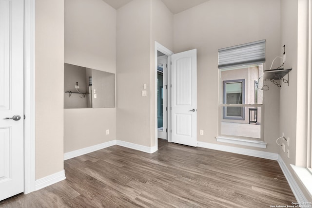 empty room with a towering ceiling, baseboards, and wood finished floors