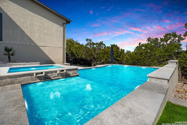 pool at dusk with an outdoor pool and an in ground hot tub