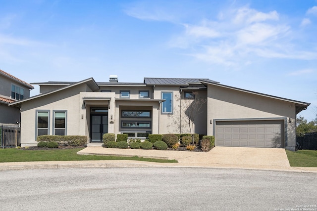 view of front of house with metal roof, an attached garage, driveway, stucco siding, and a standing seam roof