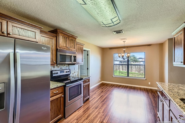 kitchen featuring light stone counters, stainless steel appliances, visible vents, dark wood-style floors, and pendant lighting