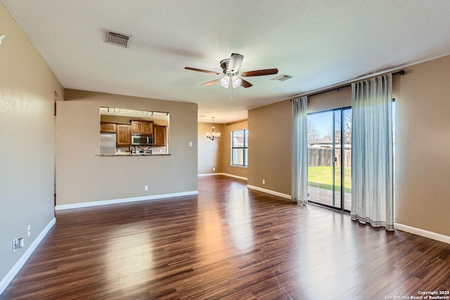 unfurnished living room with dark wood-style floors, visible vents, and ceiling fan with notable chandelier