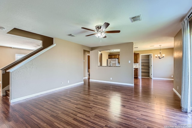 unfurnished living room featuring dark wood-style floors, ceiling fan with notable chandelier, visible vents, and stairs