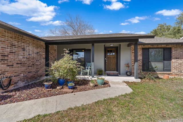 doorway to property featuring a yard, roof with shingles, a porch, and brick siding