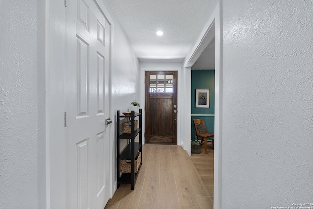 entrance foyer with light wood-type flooring, a textured wall, and a textured ceiling