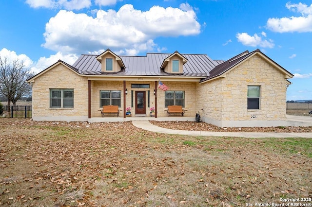 view of front facade featuring stone siding, a standing seam roof, metal roof, and fence