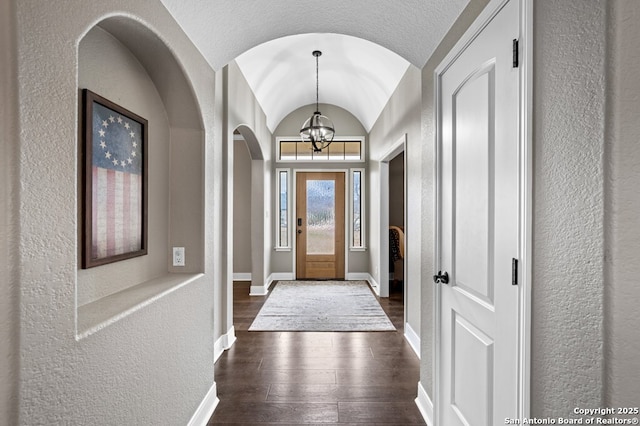 entrance foyer featuring dark wood-style flooring, a notable chandelier, a textured wall, vaulted ceiling, and baseboards