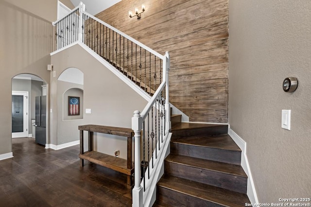 stairs with arched walkways, a high ceiling, wood finished floors, and baseboards