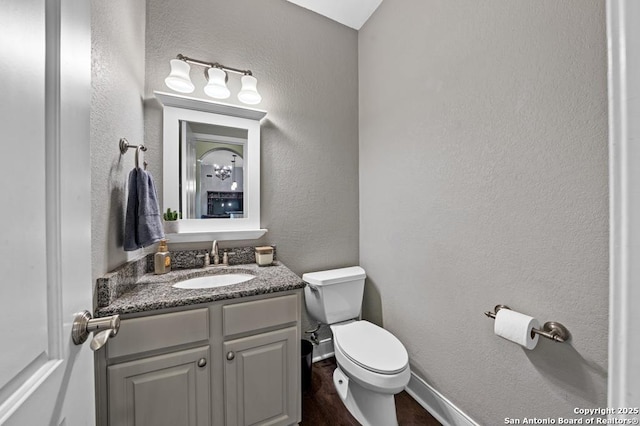 half bath featuring a textured wall, toilet, wood finished floors, vanity, and baseboards