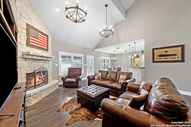 living area featuring an inviting chandelier, a stone fireplace, wood finished floors, high vaulted ceiling, and baseboards