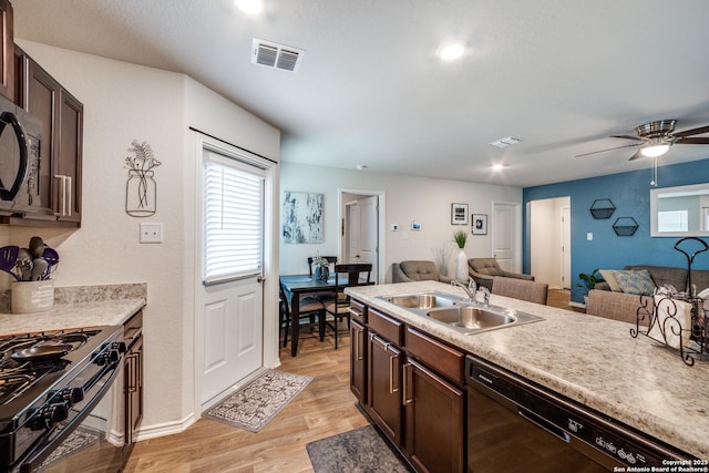 kitchen featuring visible vents, light wood-style flooring, open floor plan, black appliances, and a sink