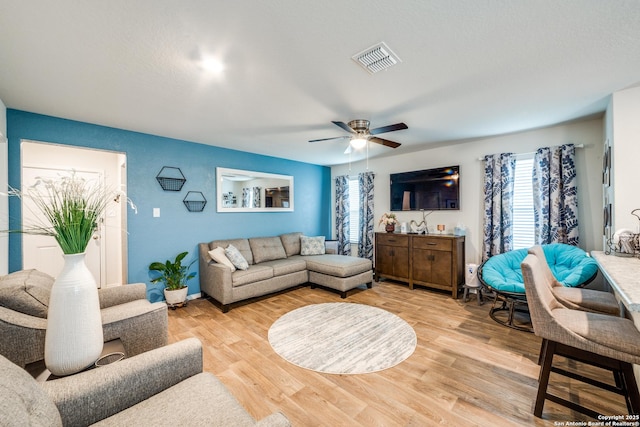 living room with light wood finished floors, visible vents, and a ceiling fan