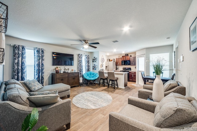 living room featuring a ceiling fan, light wood-style flooring, visible vents, and a textured ceiling