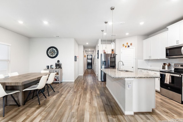 kitchen featuring a center island with sink, appliances with stainless steel finishes, light wood-style floors, a sink, and light stone countertops