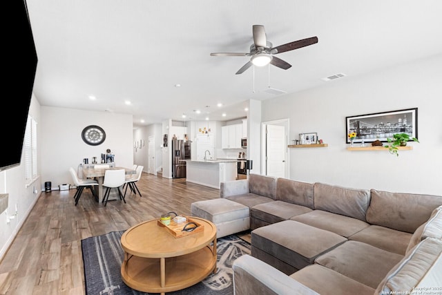 living room with light wood-type flooring, ceiling fan, visible vents, and recessed lighting