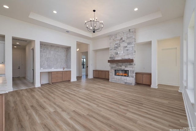 unfurnished living room with a tray ceiling, a stone fireplace, and built in desk