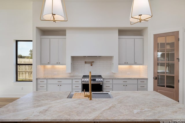 kitchen with light stone countertops, white cabinetry, decorative backsplash, and stainless steel range with gas stovetop