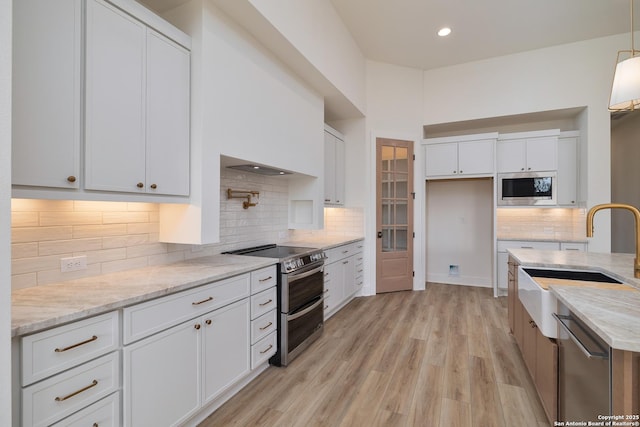 kitchen with decorative backsplash, stainless steel appliances, light wood-type flooring, white cabinetry, and a sink