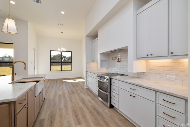 kitchen with light wood finished floors, tasteful backsplash, range with two ovens, hanging light fixtures, and a sink