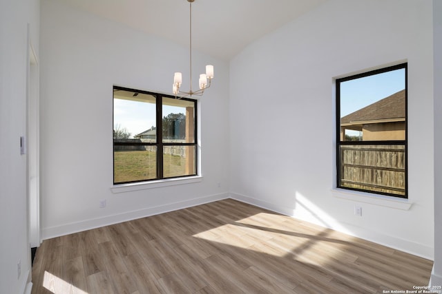 unfurnished room with baseboards, vaulted ceiling, a notable chandelier, and wood finished floors