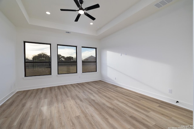 empty room featuring light wood-style flooring, a raised ceiling, visible vents, and baseboards