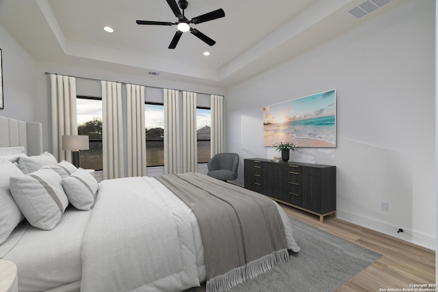 bedroom featuring light wood-style flooring, recessed lighting, visible vents, baseboards, and a tray ceiling