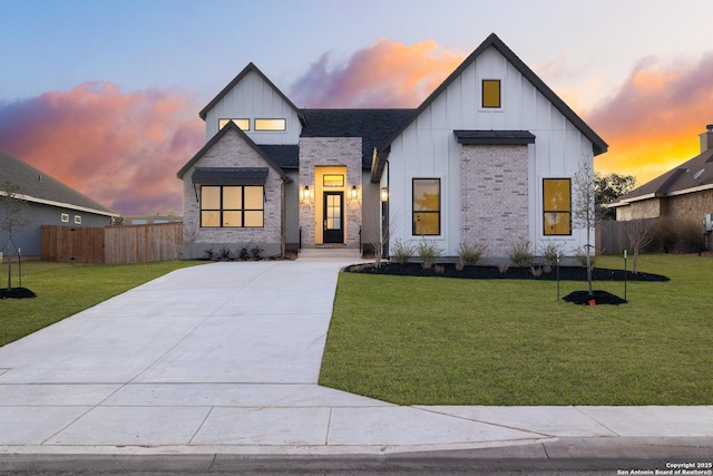 modern farmhouse style home featuring brick siding, board and batten siding, fence, and a lawn