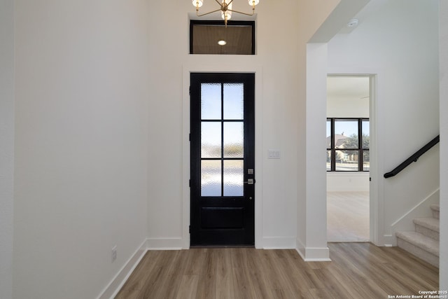 entryway with stairs, baseboards, an inviting chandelier, and light wood-style floors