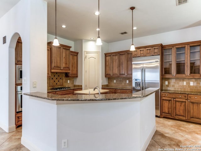 kitchen with built in appliances, visible vents, an island with sink, and brown cabinetry