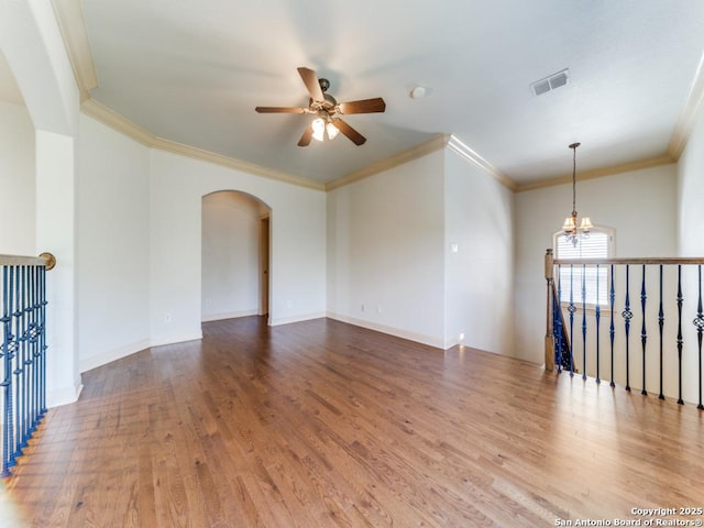 empty room with ornamental molding, arched walkways, visible vents, and wood finished floors