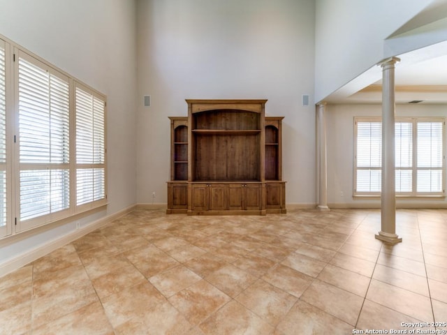 unfurnished living room with baseboards, decorative columns, a high ceiling, and light tile patterned floors