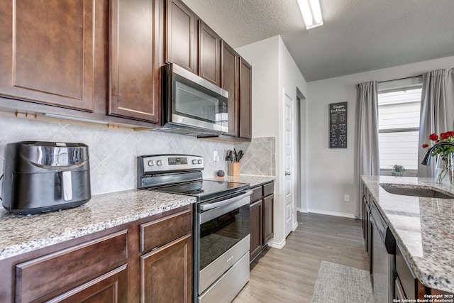 kitchen with backsplash, light stone countertops, stainless steel appliances, light wood-style floors, and a sink