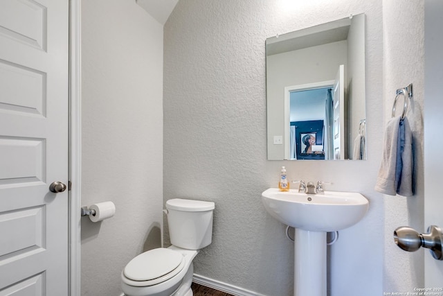 bathroom featuring a textured wall, toilet, and baseboards