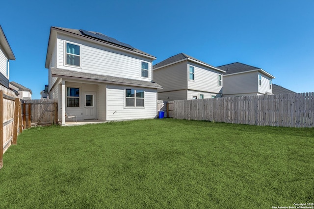 back of house with roof mounted solar panels, a fenced backyard, and a yard