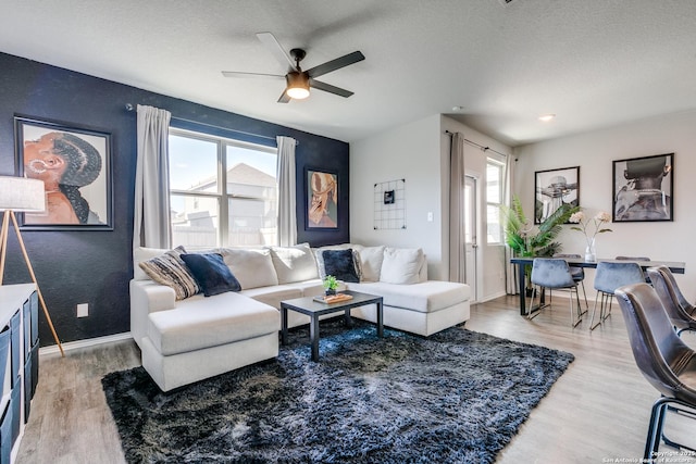 living room with ceiling fan, a textured ceiling, baseboards, and wood finished floors