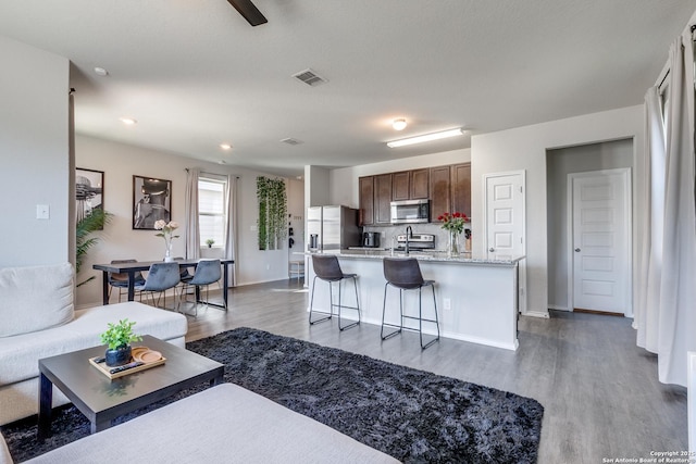 kitchen with a center island with sink, stainless steel appliances, visible vents, wood finished floors, and a kitchen bar