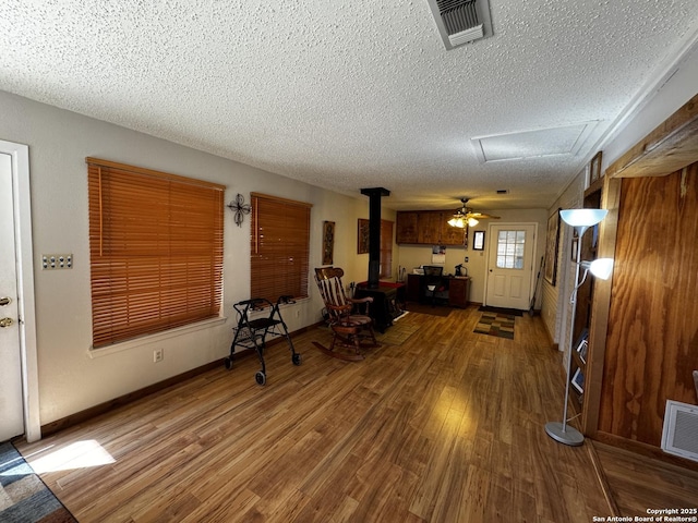 interior space featuring a wood stove, visible vents, a textured ceiling, and wood finished floors