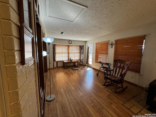 unfurnished room featuring visible vents, attic access, a textured ceiling, wood finished floors, and baseboards