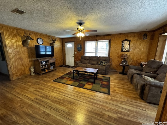 living room featuring visible vents, wood walls, ceiling fan, a textured ceiling, and wood finished floors