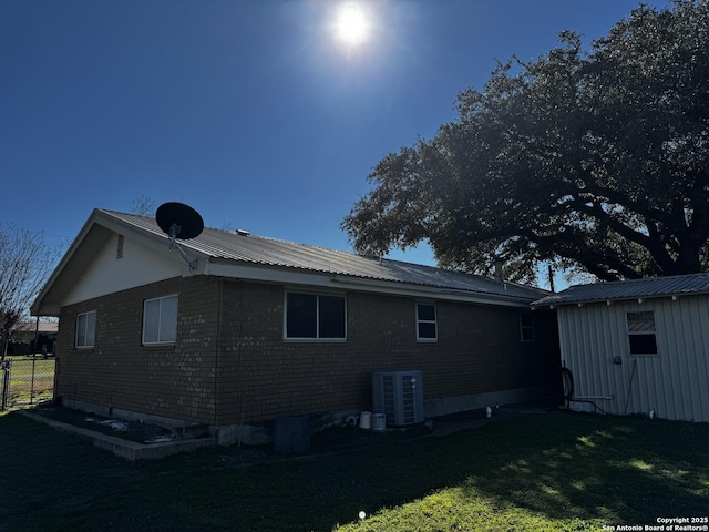 view of side of home with brick siding, central air condition unit, a lawn, metal roof, and fence