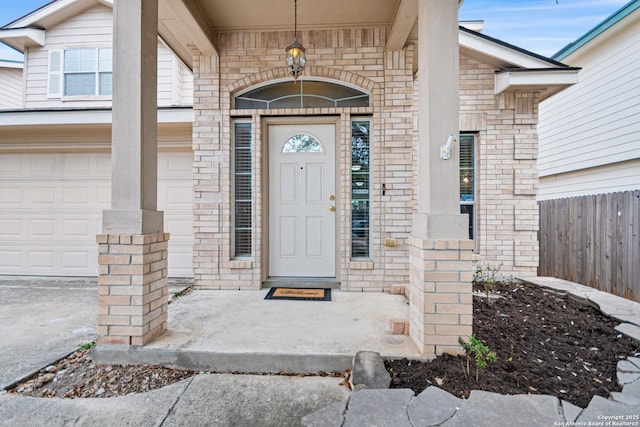 property entrance with an attached garage, fence, and brick siding