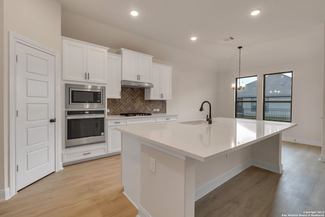 kitchen with under cabinet range hood, a sink, visible vents, appliances with stainless steel finishes, and an island with sink