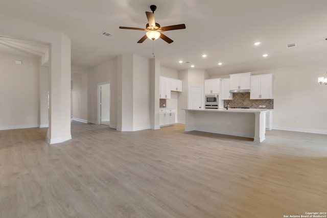 interior space featuring light wood finished floors, stainless steel microwave, decorative backsplash, open floor plan, and white cabinetry