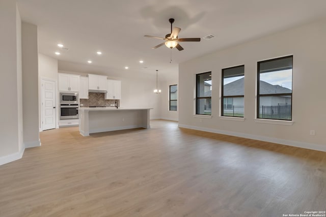 unfurnished living room with ceiling fan with notable chandelier, light wood-type flooring, visible vents, and baseboards