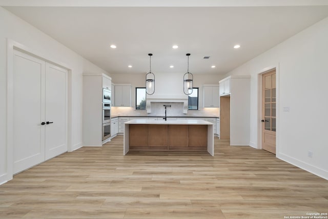 kitchen with white cabinets, light wood-style flooring, light countertops, and backsplash