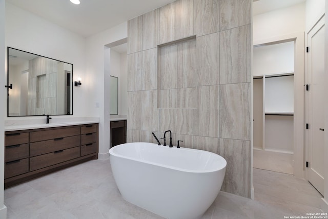 bathroom featuring tile patterned floors, a spacious closet, a freestanding bath, vanity, and tile walls